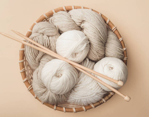 top view of yarn and knitting needles in wicker basket on beige background